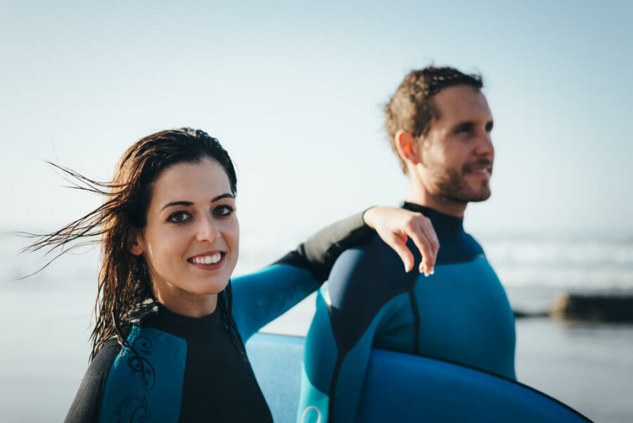 young couple in wetsuits coming out of the water