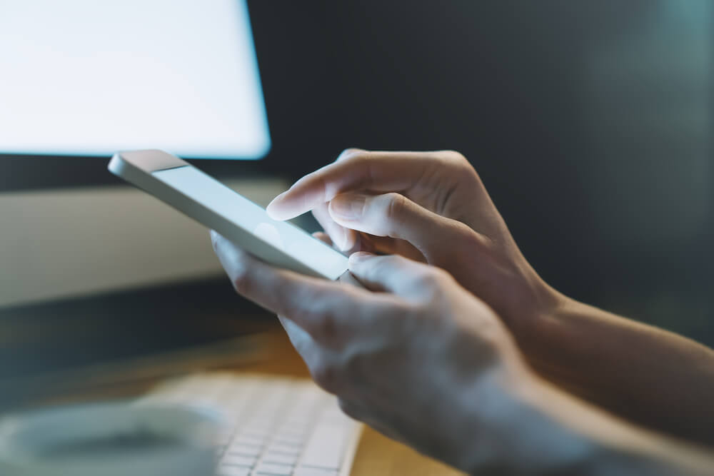 Person using a smart phone in front of a computer