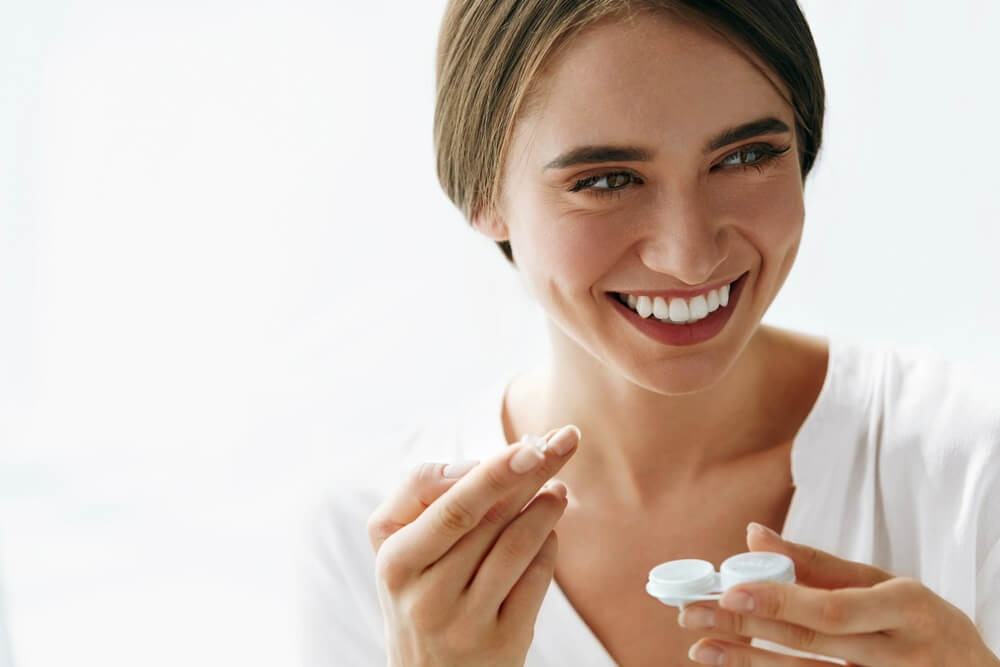 Smiling woman holding contact lenses